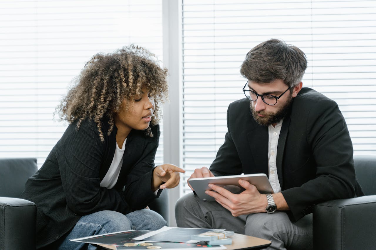 Two colleagues in a business setting discussing ideas using a tablet for planning.